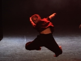 Bildet viser en solodanser som gjør ett høyt hopp. Hun bøyer samtidig beina inn under seg.