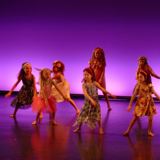 Bilde av dansere på scenen i Sandnes kulturhus. Lyssettingen er lilla og de 12 danserne på 8-9 år har på seg sommerkjoler. 