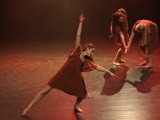 Bildet viser ei som danser samtidsdans på scenen. Hun har på seg brun kjole og strekker hele kroppen sin ut til siden. 