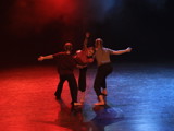 Bildet viser en trio som danser samtidsdans på scenen. Lyset gir rød stemning.