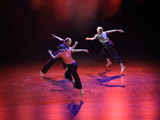 Bildet viser tre dansere som løper i ring på scenen.  Gulvet er lyssatt i rosa. 