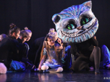 [Bildet viser FoTa dans på scenen i  Alice in wonderland. Her ser du katten. Den har stort hode og lang hale. FoTa danserne er svartkledde og utgjør kroppen til katten.] 