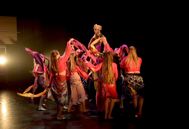 Bildet viser dansere på scenen i forestillingen det magiske teppet. De har på seg fargerike magedgnserkostyme. I midten står en prins med gullhatten. 