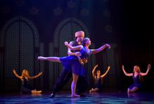 [Bildet viser en gutt og ei jente som danser sammen på scenen. Jenta holdes i en balllettposisjon av gutten. Han støtter henne. Beinet til jenta er 90 grader rett ut bak i en arabesque posisjon. Hun har blå glitterkjole på seg, og gutten har svarte klær og gullhatten. Han ser ut som en prins.] 