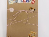 Scrapbook i brun papp med fargerike bokstaver og rosa sløyfe på midten. 
