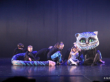 [Bildet viser FoTa dans på scenen i  Alice in wonderland. Her ser du katten. Den har stort hode og lang hale. FoTa danserne er svartkledde og utgjør kroppen til katten.] 